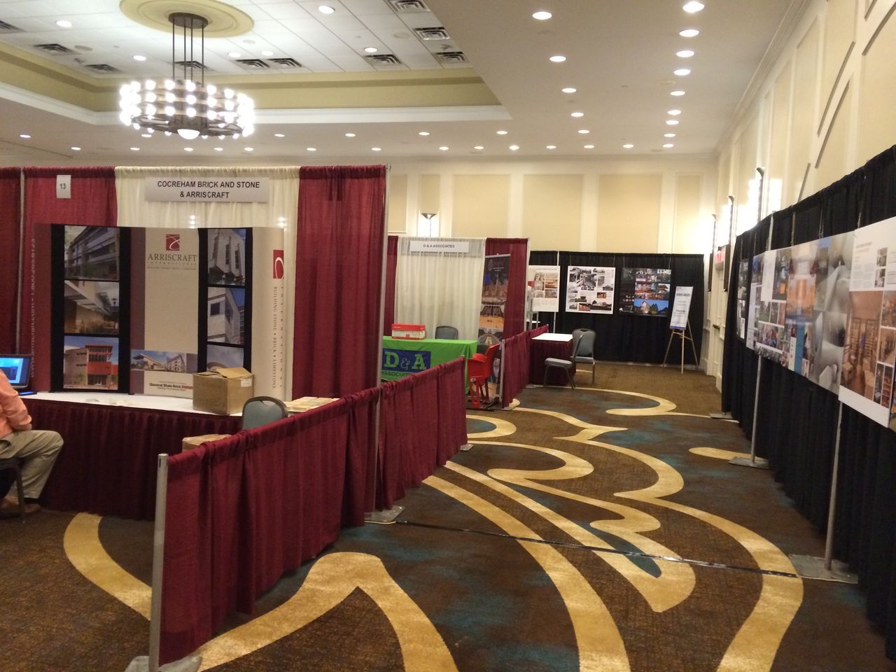Exhibit hall with maroon and black pipe and drape booths on patterned carpet